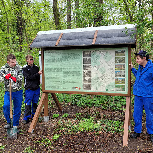 3 Auszubildende beim Aufstellen eines Parkschild / Infotafel
