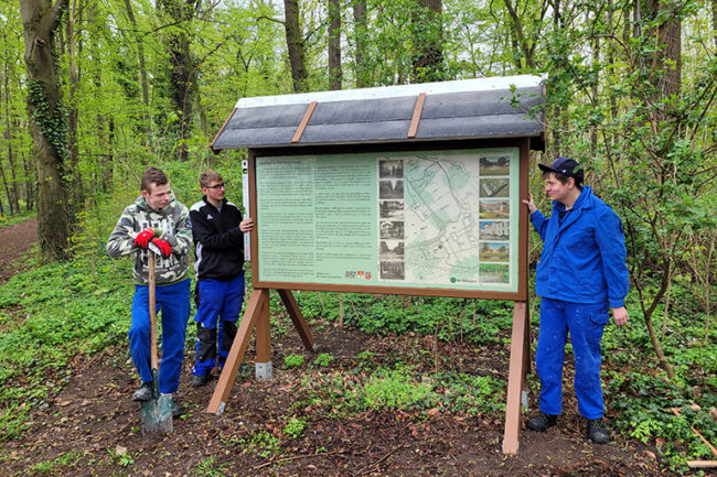 3 Auszubildende beim Aufstellen eines Parkschild / Infotafel