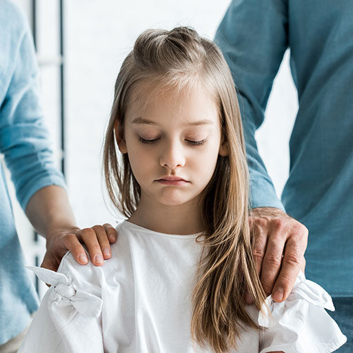 Traurig nach unten schauendes Kind mit den Händen der Eltern auf den Schultern