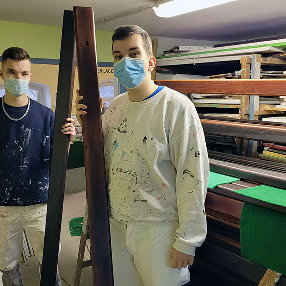 2 Auszubildende mit gestrichenen Holzplanken in der Hand