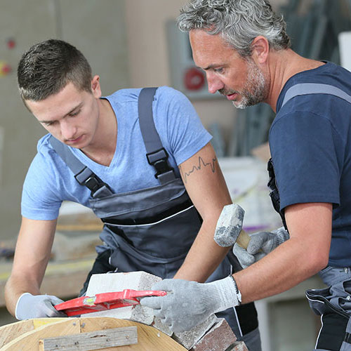 Ausbilder und Auszubildender vermessen die Ausrichtung eines Steins