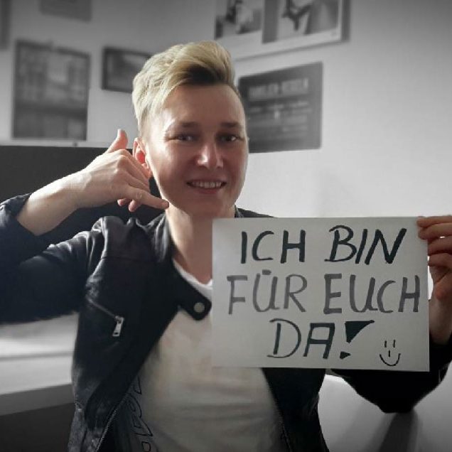 Mitarbeiterin mit Papierschild Ich bin für euch da und die Finger zum Telefonhörer gebildet