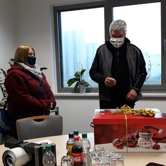 Gruppe von Menschen mit Mundschutz vor einem Weihnachtspaket