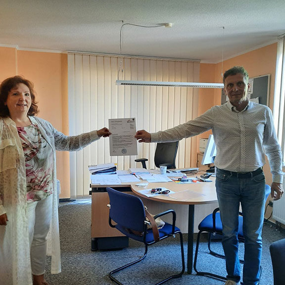Frau Heusch und Herr Kogel halten das offizielle Schreiben in der Hand