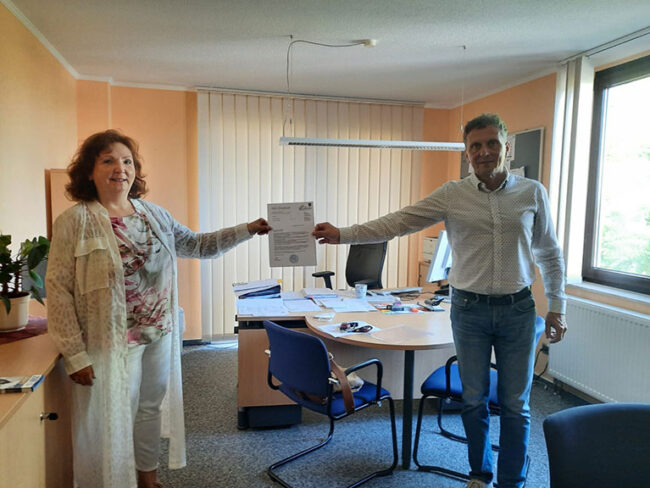 Frau Heusch und Herr Kogel halten das offizielle Schreiben in der Hand